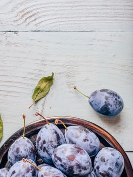 Ripe plums on metal plate over light wooden surface. Copy space