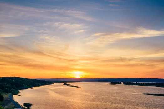 Summer sunset on river shore with orange sky.