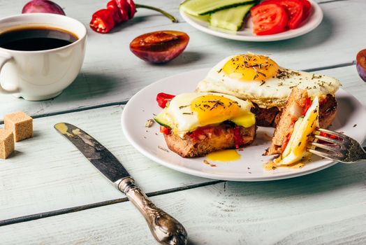 Sandwiches with vegetables and fried egg on white plate, cup of coffee and some fruits over wooden background.