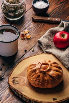 Rustic breakfast with traditional tatar pastry elesh, herbal tea in metal mug, apple and boiled eggs over dark wooden surface