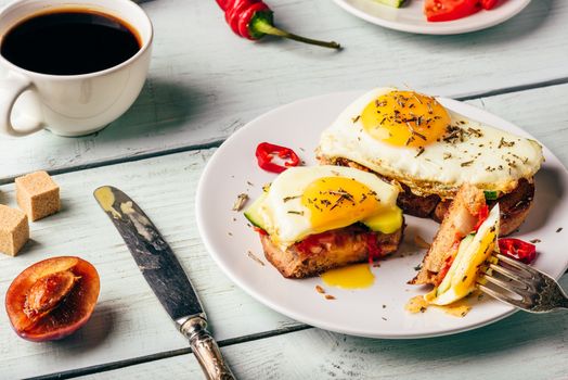 Breakfast toasts with vegetables and fried egg on white plate, cup of coffee and some fruits over wooden background. Clean eating food concept.