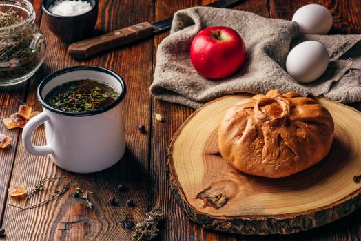 Rustic breakfast with traditional tatar pastry elesh, herbal tea in metal mug, apple and boiled eggs over dark wooden surface