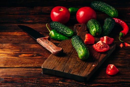 Fresh cucumbers, tomatoes and chili peppers on cutting board for preparing salad.