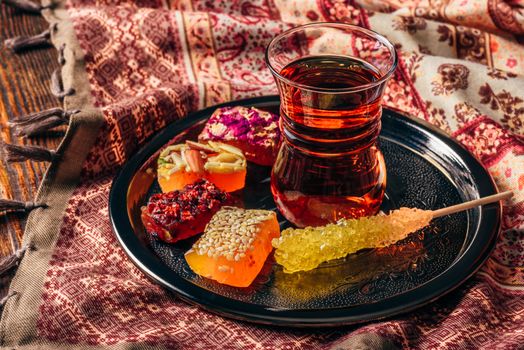 Tea in armudu glass with oriental delight rahat lokum on metal tray over wooden surface and tablecloth