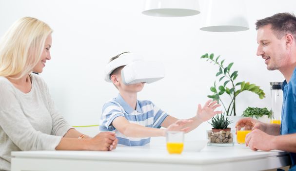 Happy caucasian family at home at dinning table, having fun playing games using virtual reality headset.