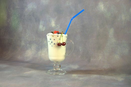 Tall glass cup with milkshakes with a straw and berries.