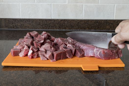 man with nife cutting a nice lean piece of beef is cut into pieces in the kitchen to prepare a meat dish