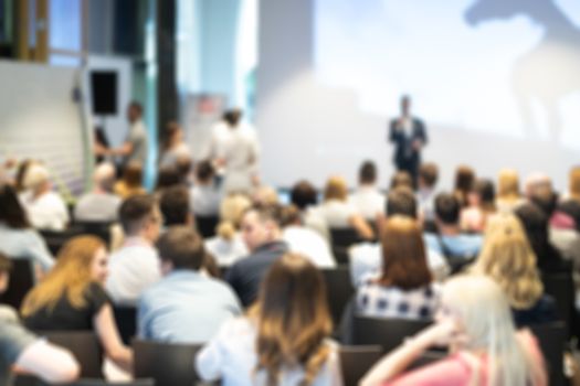 Business and entrepreneurship symposium. Speaker giving a talk at business meeting. Audience in conference hall. Rear view of unrecognized participant in audience.