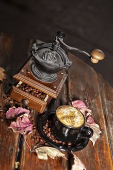 Coffee mill, beans, cup of coffee and autumn leaves on a wooden desk