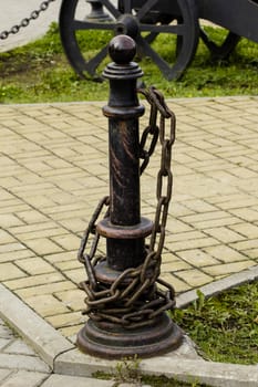 

Metal rack with chain on the background of paving slabs.