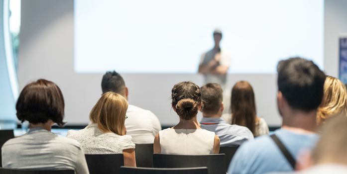 Male speaker giving a talk in conference hall at business event. Audience at the conference hall. Business and Entrepreneurship concept. Focus on unrecognizable people in audience.