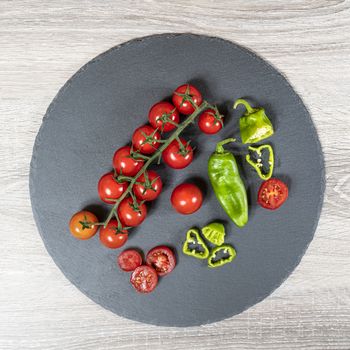 some small tomatoes and green peppers on a stone plate