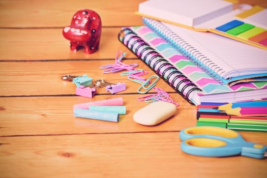 Close up shot of pastel colored girl school stationary on wooden background.