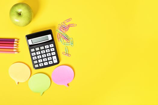 Math accessories for class. Flat lay of calculator, sticky notes and apple on yellow background.