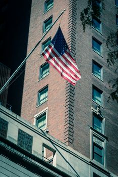Vintage tone proudly display of American flag outside of government building near Union Station in downtown Chicago, Illinois. Flying stars and stripes flag with historical brick building facade