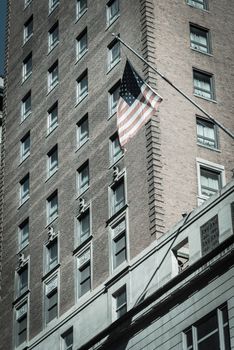 Vintage tone proudly display of American flag outside of government building near Union Station in downtown Chicago, Illinois. Flying stars and stripes flag with historical brick building facade