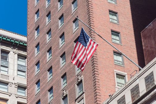 Proudly display of American flag outside of government building near Union Station in downtown Chicago, Illinois. Flying stars and stripes flag with historical brick building facade background