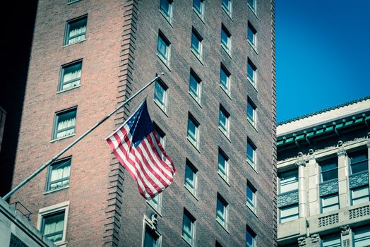 Vintage tone proudly display of American flag outside of government building near Union Station in downtown Chicago, Illinois. Flying stars and stripes flag with historical brick building facade