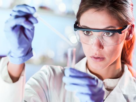 Life scientists researching in laboratory. Focused female life science professional pipetting solution into the glass cuvette. Lens focus on researcher's eyes. Healthcare and biotechnology concept.