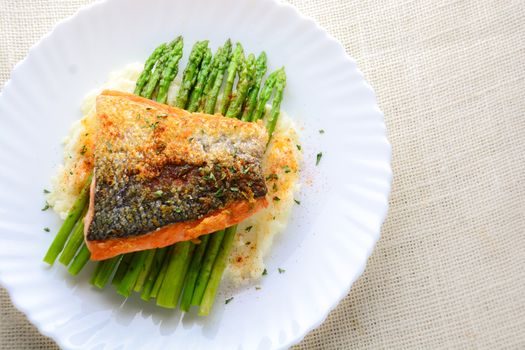 Grilled salmon garnished with asparagus and herbs and mashed potatoes, served on white plated.
