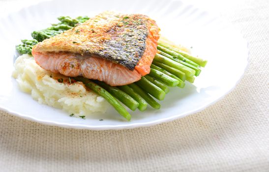 Grilled salmon garnished with asparagus and herbs and mashed potatoes, served on white plated.
