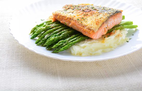 Grilled salmon garnished with asparagus and herbs and mashed potatoes, served on white plated.
