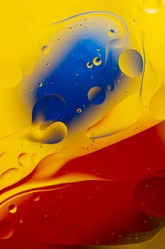Abstract oil spots in motion on water on blurred yellow background. Red and blue spots on blurred background. Photo with small depth of field.