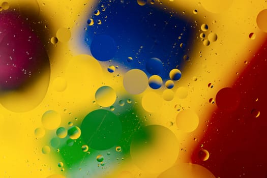 Abstract oil spots in motion on water on blurred yellow background. Red, green, purplee and blue spots on blurred background. Photo with small depth of field.