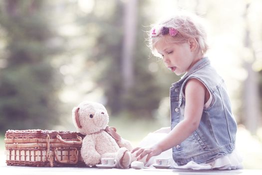 Pretty girl playing with teddy bear outdoors