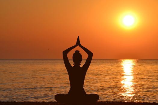 Silhouette of young woman practicing yoga on the beach at sunrise