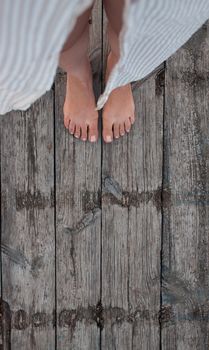 Beautiful female bare bare tanned legs with pink pedicure on wooden beach flooring. Top view, copy space.