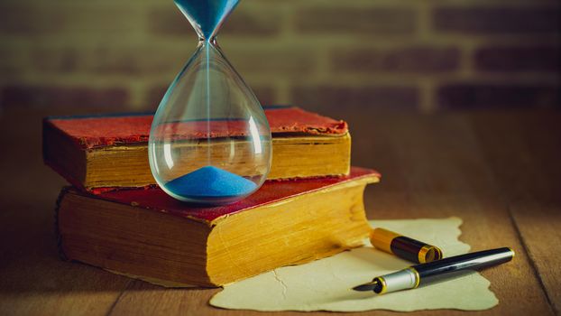 Sand clock with old books and pen with paper map on the wooden table. Concept of travel planning.