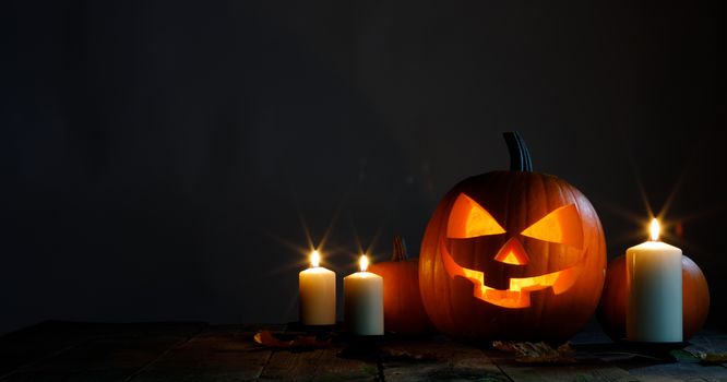 Halloween pumpkin head jack o lantern candles and dry maple leaves on wooden background
