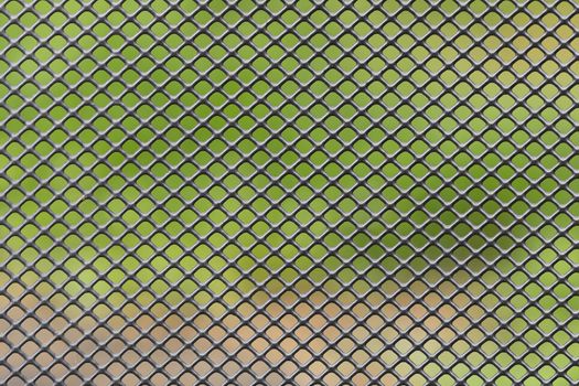 Metal grid diagonally crossed with blurred green brown background
