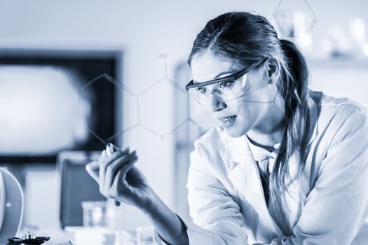 Portrait of a confident female health care expert in life science laboratory writing structural chemical formula on a glass board. Healthcare and modern life science concept. Blue toned image.