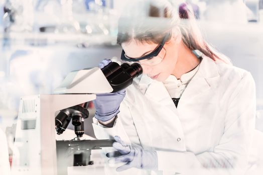 Life scientists researching in laboratory. Focused female young scientist microscoping in scientific working environment. Healthcare science and biotechnology.