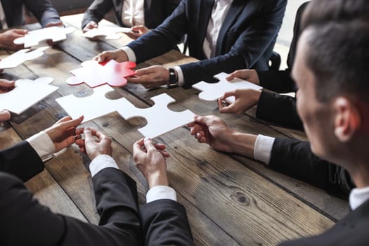 Business people and puzzle on wooden table, teamwork concept
