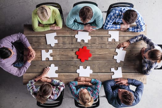 Business people and puzzle on wooden table, teamwork concept
