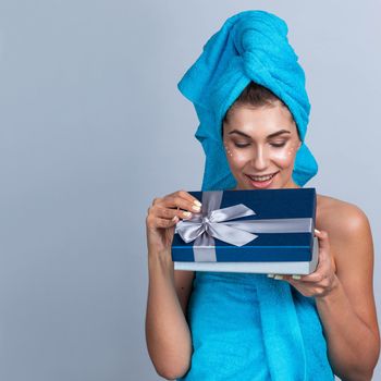 Beautiful young woman after shower with towel on head and creme on her face open beauty holiday gift