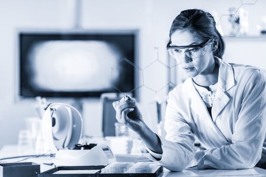 Portrait of a confident female health care expert in life science laboratory writing structural chemical formula on a glass board. Healthcare and modern life science concept. Blue toned image.