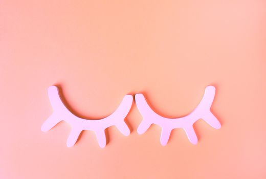 White wooden closed eyes with eyelashes in neon pink light on pastel background. Stylish wall decor. Top view, flat lay. Concept of vivid sweet dreams. Accessories for kids room. Minimal style.