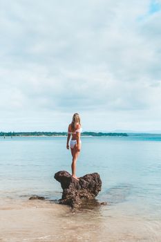 Woman in bikini standing on a rock surrounded by the ocean