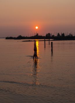 girl doing a handstand in the water during sunset with the harbor of hellevoetsluis and the boats as background