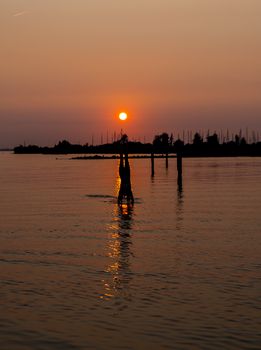 girl doing a handstand in the water during sunset with the harbor of hellevoetsluis and the boats as background