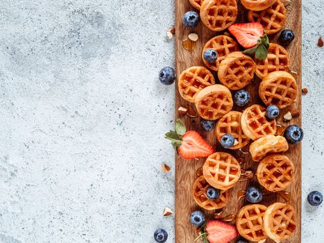 Small round delicious soft belgian waffles on cutting board. Fresh belgian waffles with berries and caramel sauce top view. Copy space for text or mock up