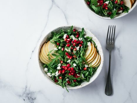 Vegan salad bowl with arugula, pear, pomegranate, coconut crumble or cottage cheese on marble tabletop. Vegan breakfast, vegetarian food, diet concept. Top view or flat lay.