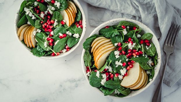 Fresh salad with baby spinach, pear, pomegranate and cottage cheese. Two bowls with delicious summer fruit salad on marble table. Copy space for text. Ideas and recipes for healthy breakfast or lunch