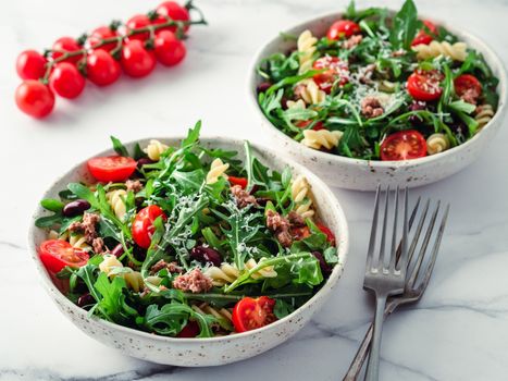 Warm salad with tuna, arugula, tomatoes, red bean, pasta. Idea and recipe for healthy lunch or dinner. Two bowls with warm salads on marble tabletop. Ideas and recipes for healthy dinner or lunch