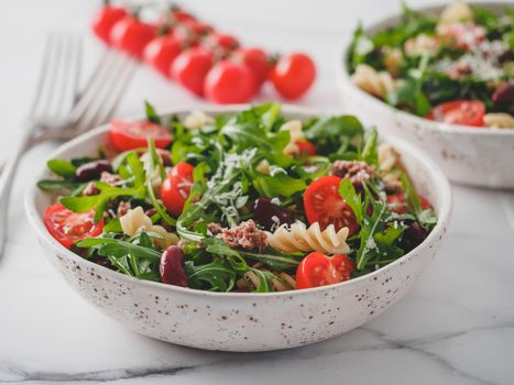 Warm salad with tuna, arugula, tomatoes, red bean, pasta. Idea and recipe for healthy lunch or dinner. Two bowls with warm salads on marble tabletop. Ideas and recipes for healthy dinner or lunch