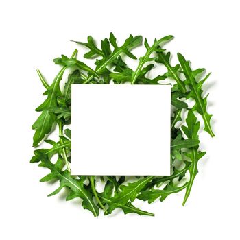 Creative layout made with arugula leaves. White paper square on heap of arugula or rucola leaves. Isolated on white with clipping path. Top view or flat lay. Copy space for text.